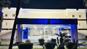 A building with a covered entrance, glass doors, and a well-maintained lawn with palm trees.