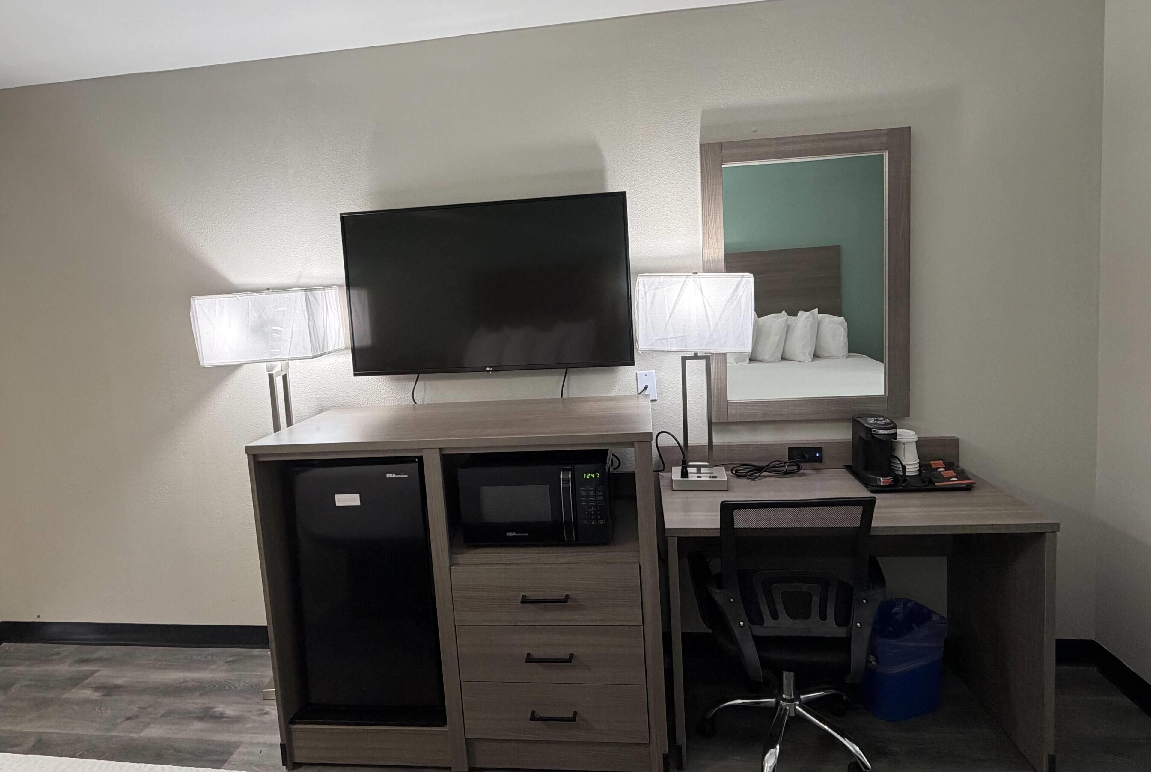 A hotel room with a desk, a flat-screen TV, a microwave, a coffee maker, and a chair.
