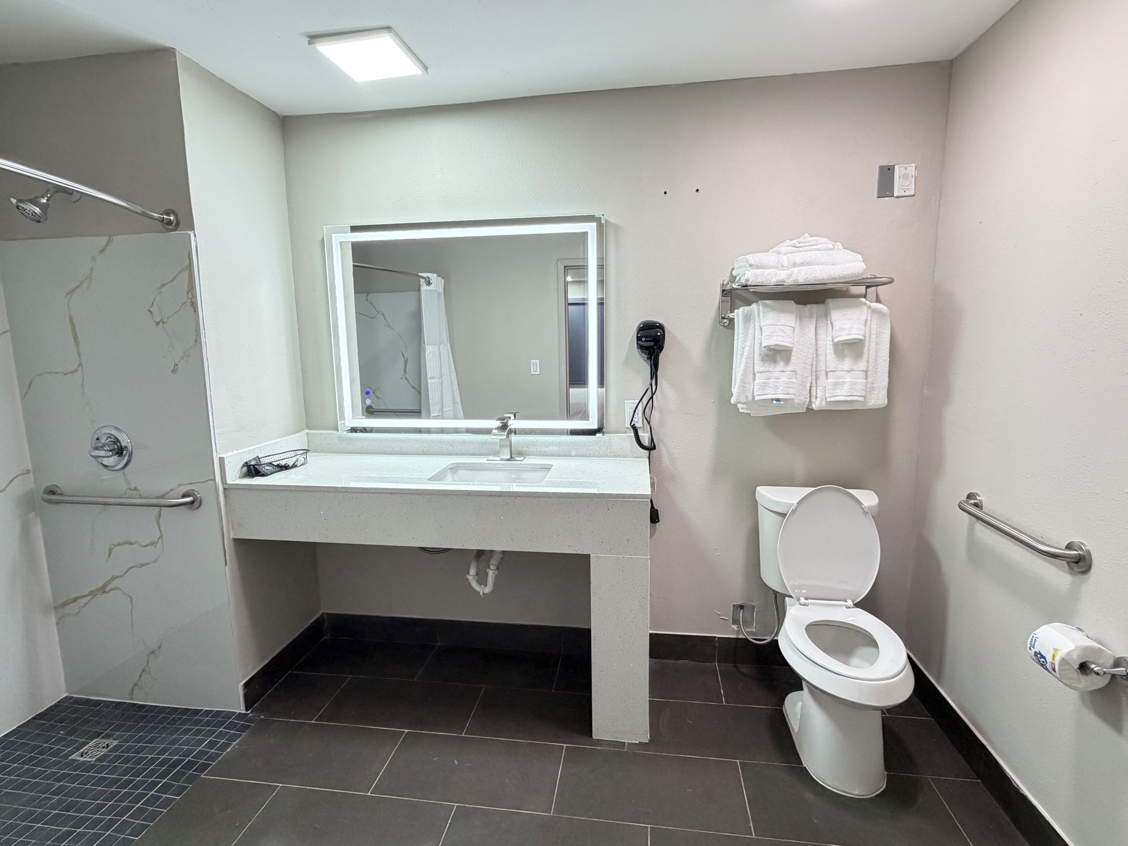 A bathroom with a shower, toilet, sink, and hand dryer.