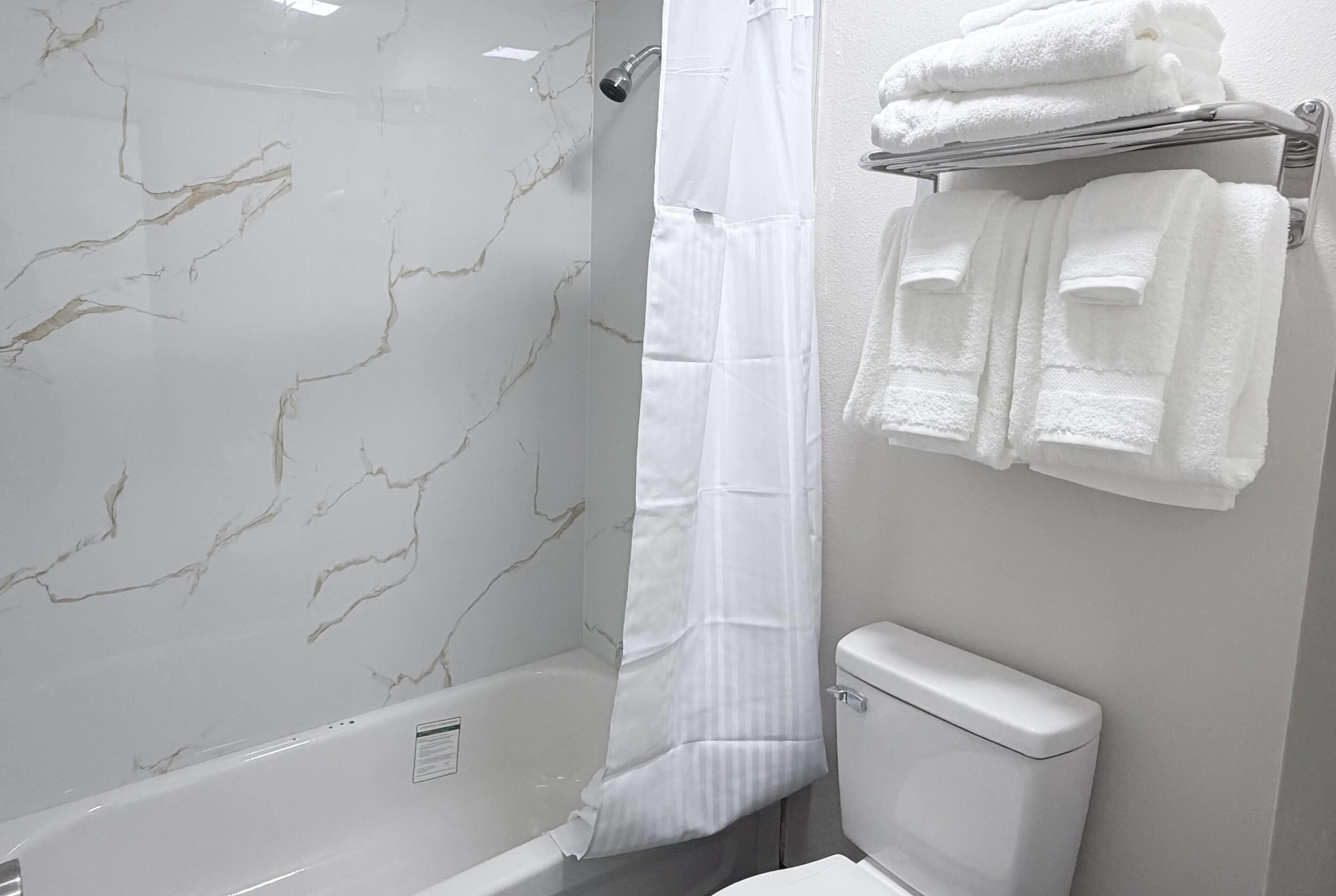 Une salle de bain avec un mur en marbre, un rideau de douche, des toilettes et un porte-serviettes avec des serviettes pliées.