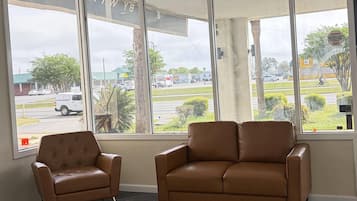 A room with two brown leather chairs, large windows with a view of a street and buildings, and a sign warning of a wet floor.