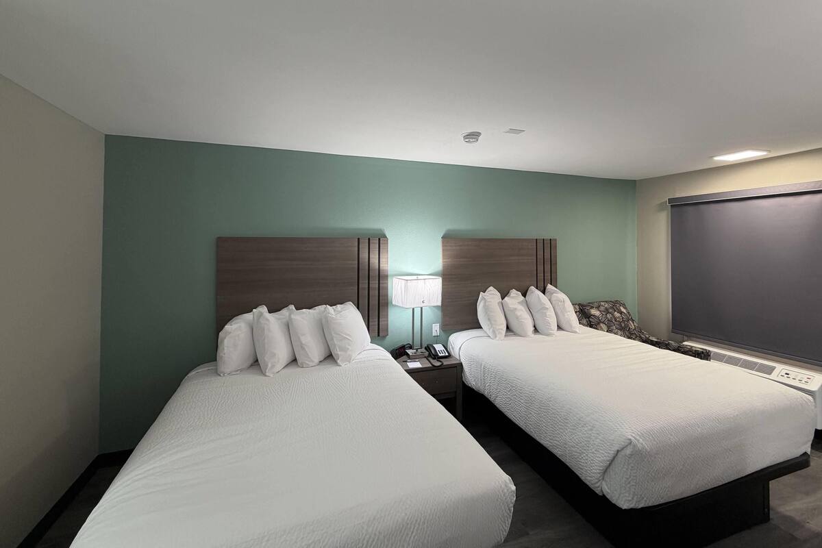 A hotel room with two beds, a nightstand with a lamp, a phone, and a window with a view.