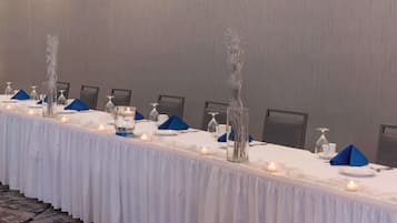 Una larga mesa de banquete con manteles blancos, servilletas azules y velas.