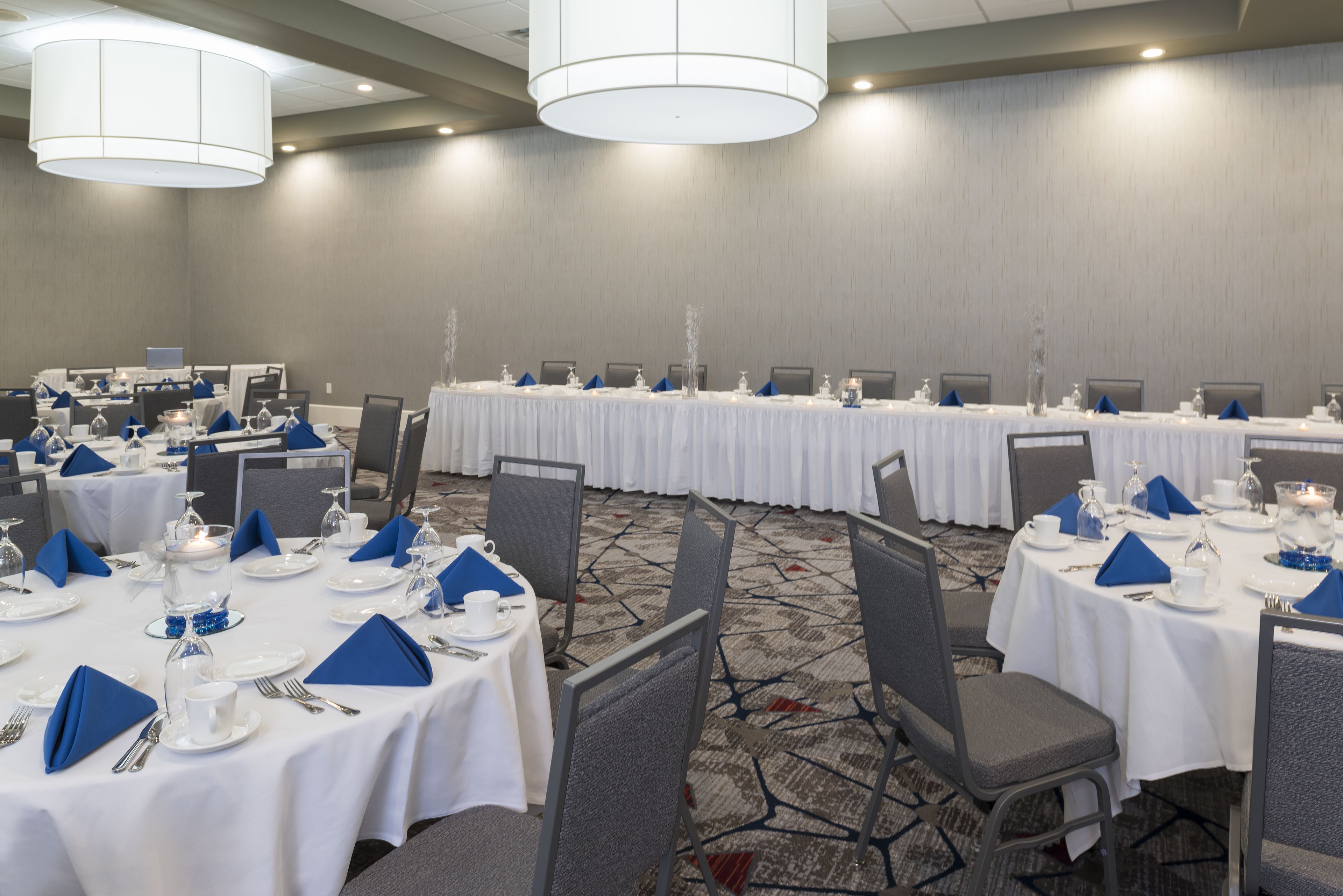 Un salón de conferencias con mesas redondas dispuestas para una reunión, equipado con sillas, mesas y centros de mesa.