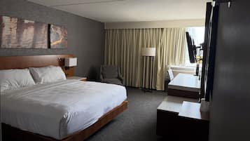 Habitación de hotel con una cama grande, un escritorio, una silla, una lámpara y vistas al exterior.