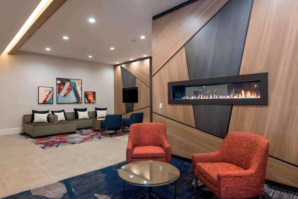 A modern lounge area with a sofa set, two red armchairs, a glass coffee table, and a wall-mounted fireplace.