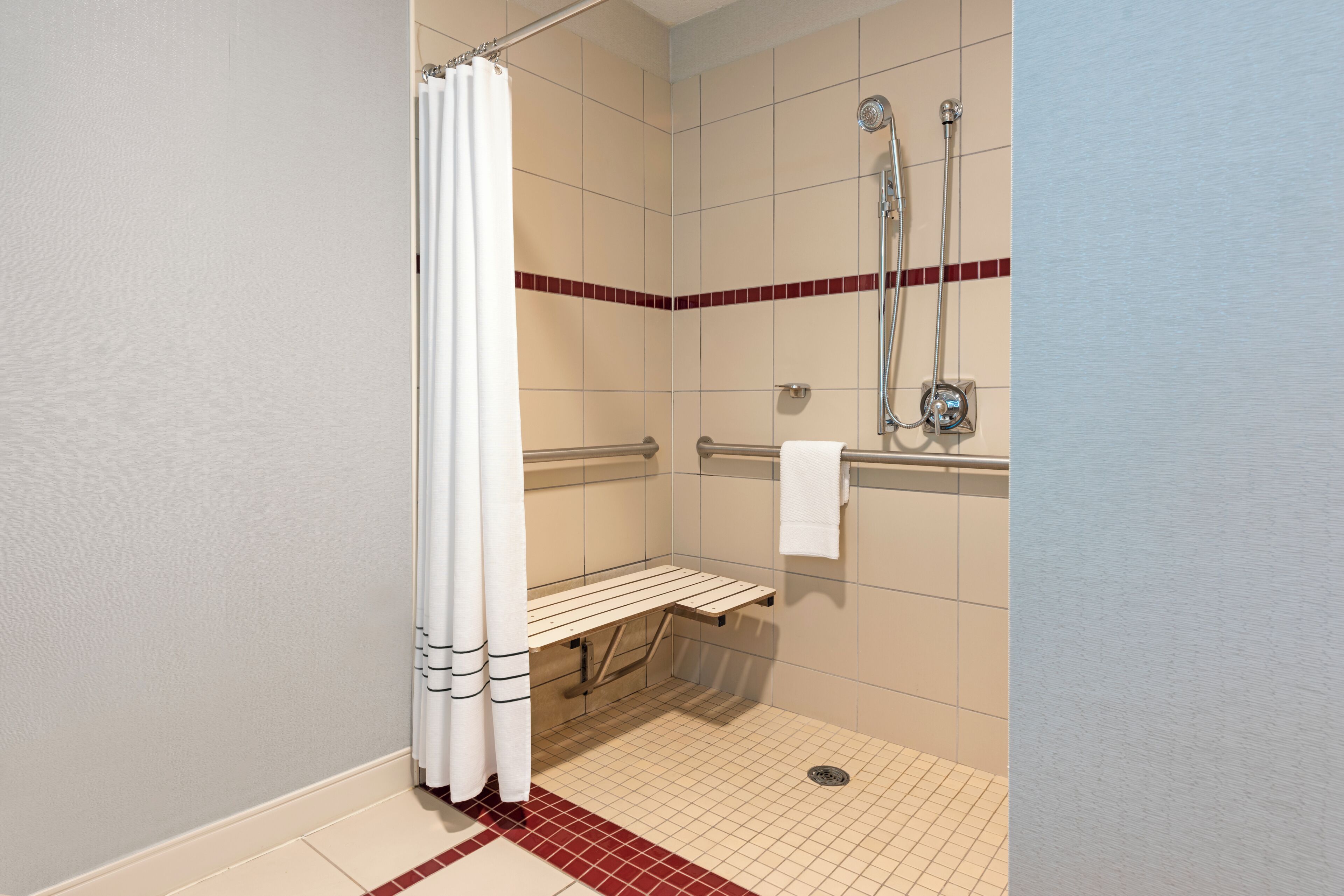 Un espace douche avec un rideau de douche blanc, un banc, une douchette à main et un porte-serviettes.