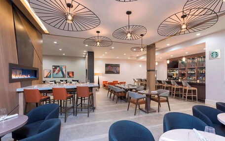 A modern restaurant with multiple dining areas, including a bar and a seating area with tables and chairs.