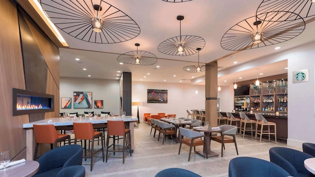 A modern restaurant with multiple dining areas, including a bar and a seating area with tables and chairs. - The Center Hotel Grand Rapids Airport (Grand Rapids)