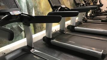 A row of Life Fitness treadmills with digital displays, in a gym with a greenish wall and a white baseboard.