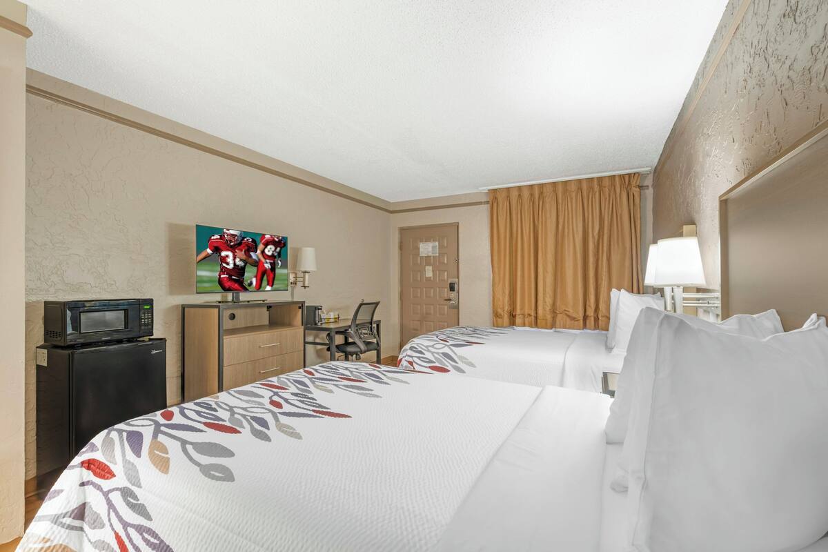 Une chambre d’hôtel avec deux lits, un bureau avec une chaise, une télévision, un four à micro-ondes et une porte avec une pancarte.