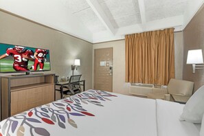 A hotel room with a bed, a TV, a desk, a chair, and a door. - Red Roof Inn Tampa Bay - St Petersburg (St. Petersburg)