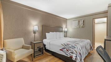 Ein Hotelzimmer mit Bett, Nachttisch, Lampe, Stuhl und einem Wandbild.