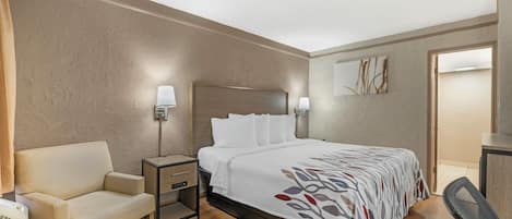 Une chambre d’hôtel comprenant un lit, une table de chevet, une lampe, une chaise et un mur orné d’un tableau.
