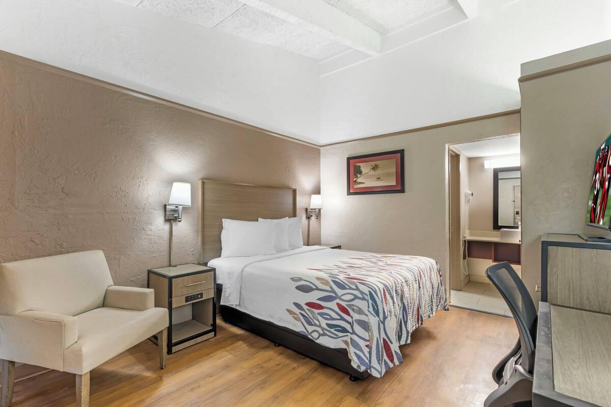 Une chambre d’hôtel comprenant un lit, une table de chevet, une lampe, une chaise, un bureau et un miroir.
