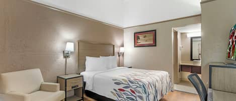 A hotel room with a bed, bedside table, lamp, chair, desk, and a mirror.