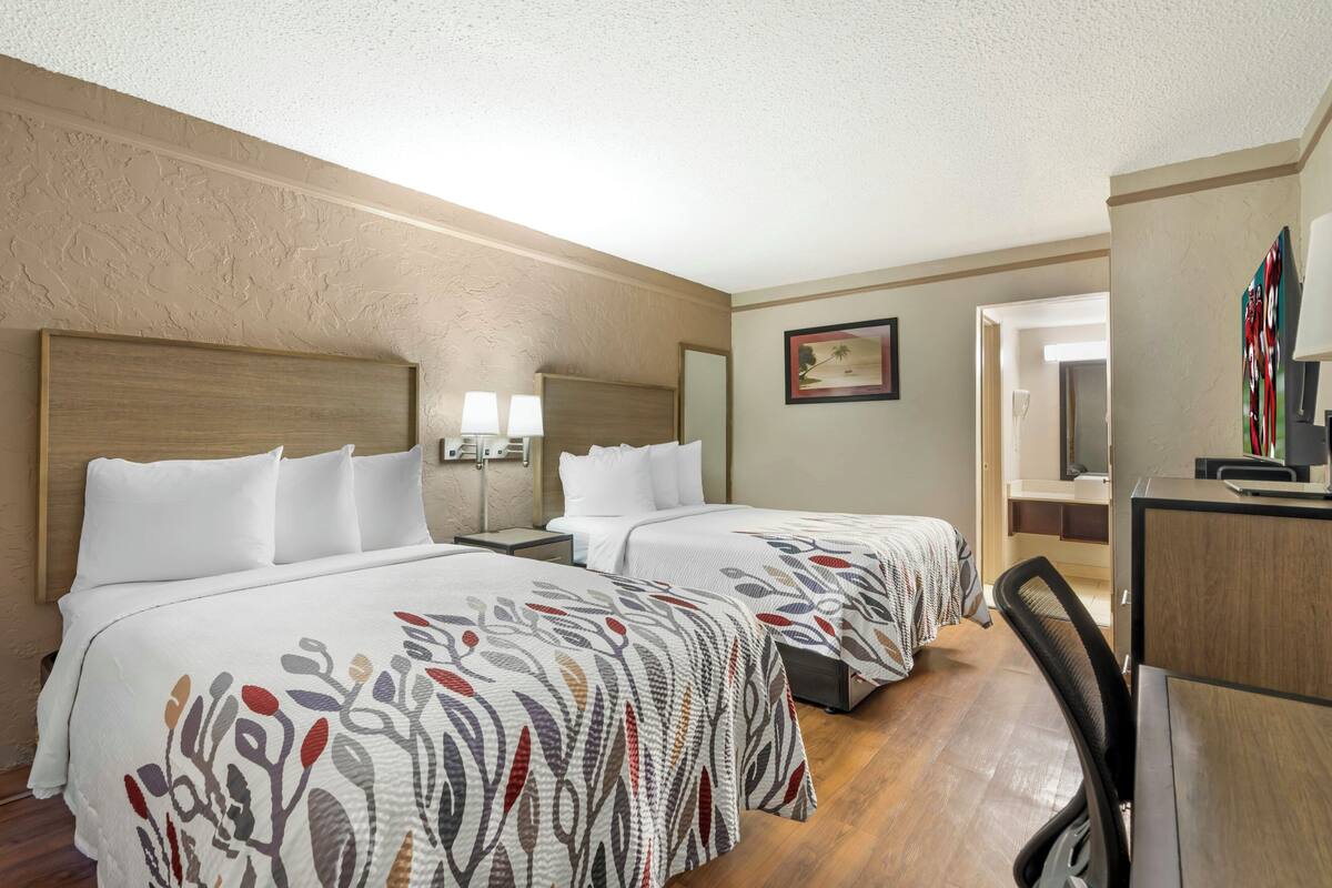 Une chambre d’hôtel avec deux lits, un bureau, une chaise, une lampe et un tableau au mur.