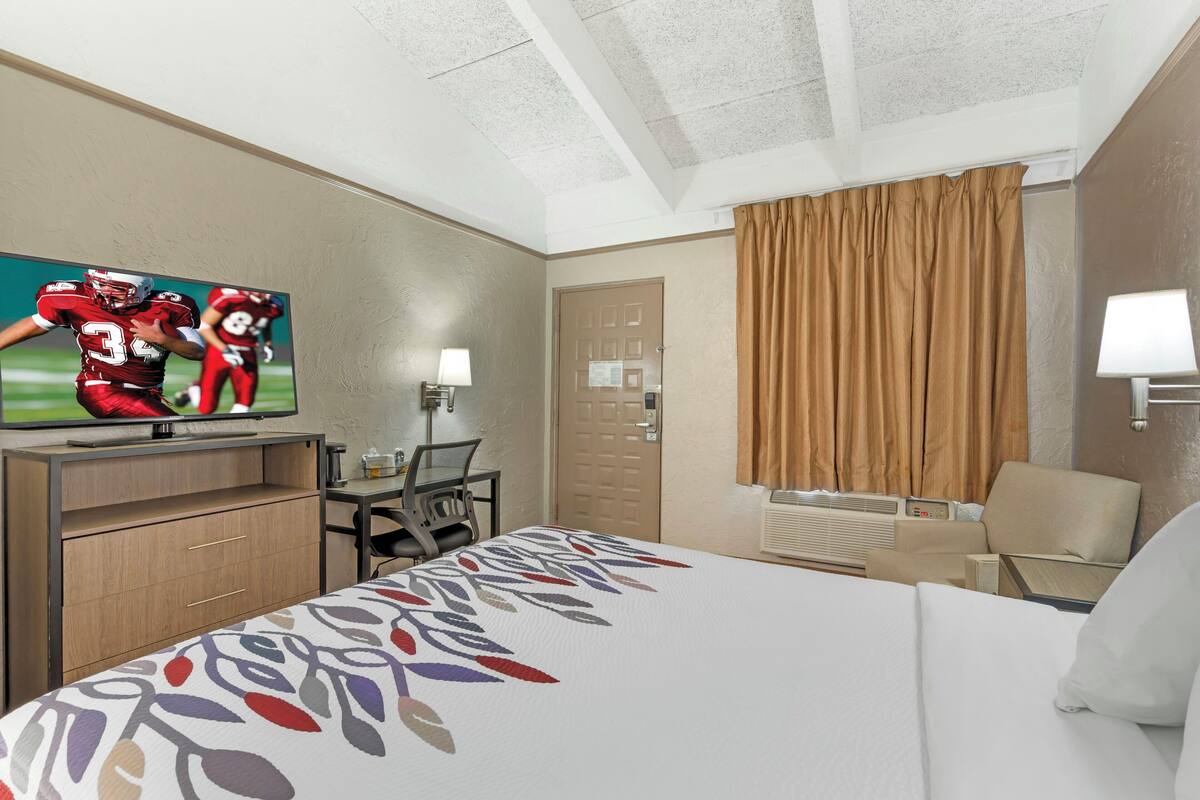 Une chambre d’hôtel avec un lit, une télévision, un bureau, une chaise et une porte.