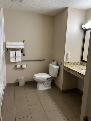 A hotel bathroom with a white toilet, a grab bar, a towel rack, and a sink with a granite countertop.