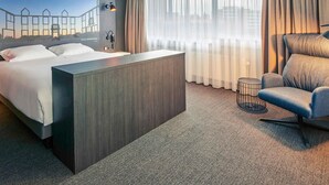 Ein modernes Hotelzimmer mit einem großen Bett, einem Schreibtisch, einem Sessel und einer Wandmalerei mit Stadtansicht.