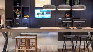 Ein moderner Empfangstresen mit zwei Computermonitoren, einer Holztischplatte und einer Sitzgelegenheit mit Hocker.