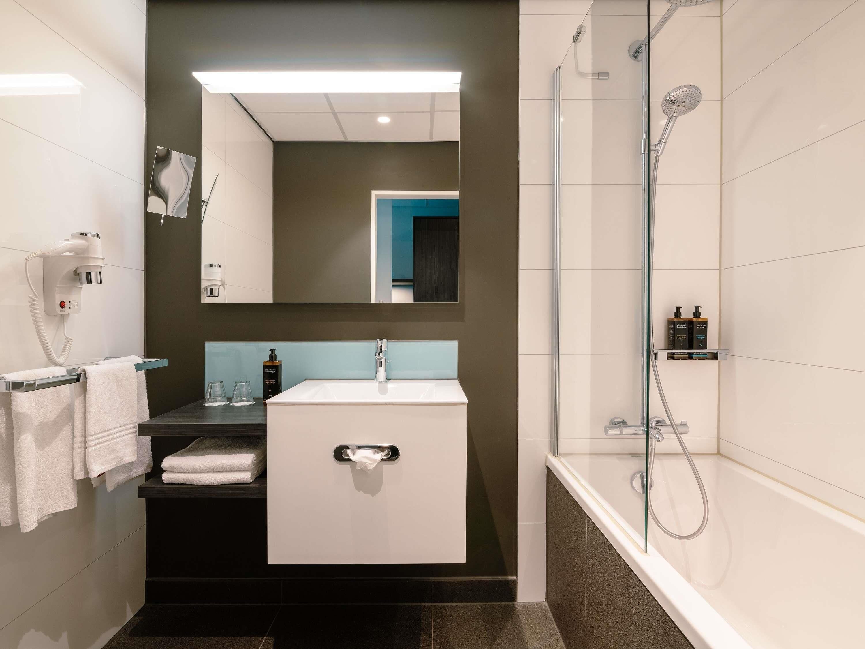 A modern bathroom with a white sink, a mirror, a towel rack, a hairdryer, and a glass-enclosed shower.