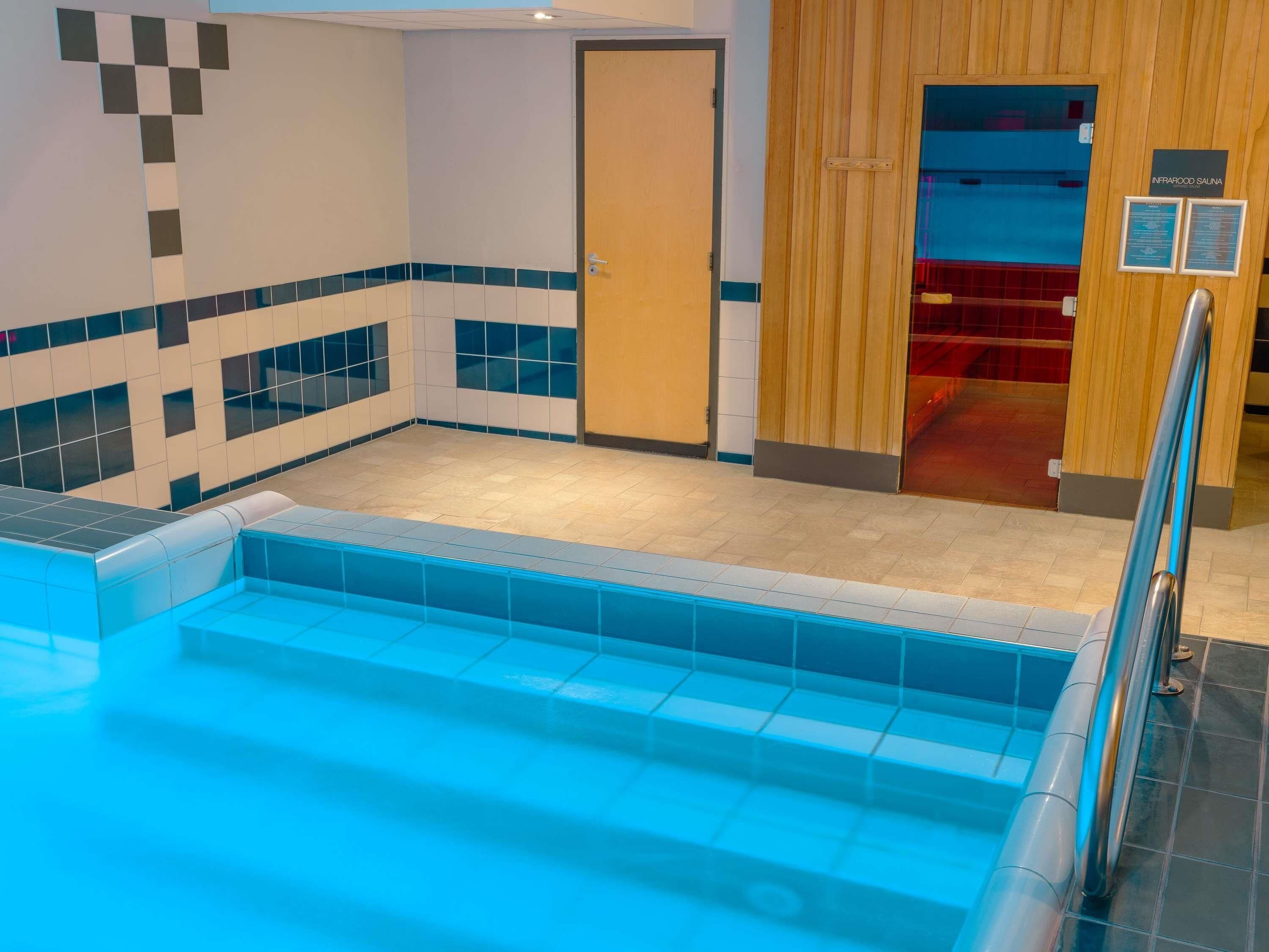 A pool area with a tiled floor, a wooden door, and a sign indicating an infrared sauna.