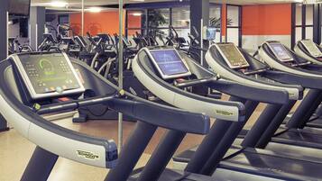 Un gimnasio con varias cintas de correr, cada una con una pantalla digital.