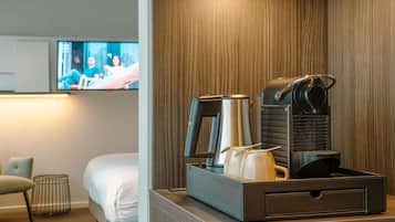 Une chambre d’hôtel équipée d’un lit, d’un téléviseur fixé au mur, d’une machine à café et d’un plateau avec une théière et des tasses.