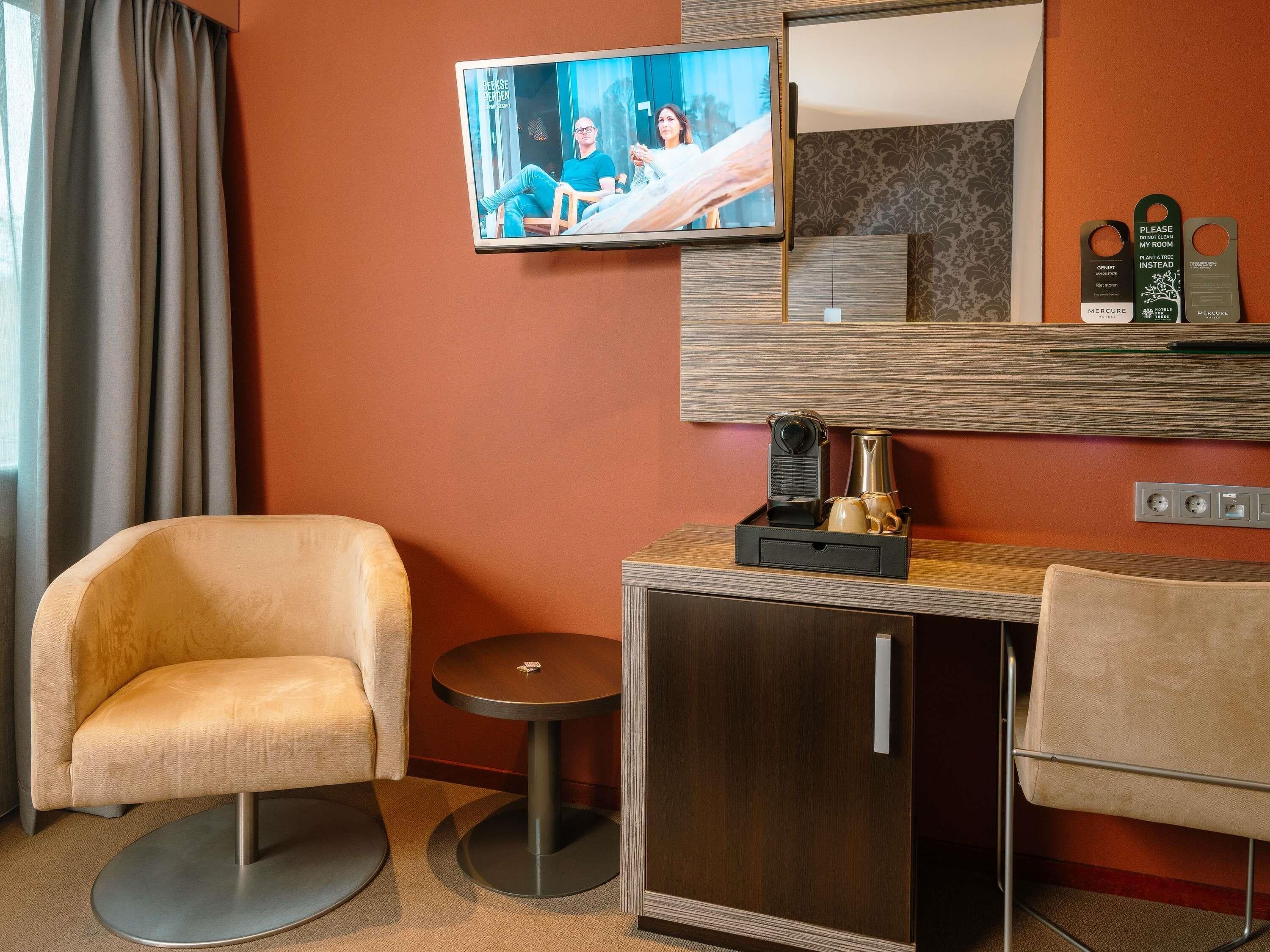 A hotel room with a TV, a small table with a coffee maker, two chairs, and a mirror.