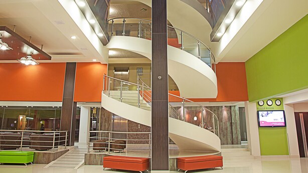 Un atrio de varios niveles con una escalera espiral central, zonas de descanso y una pantalla digital.
