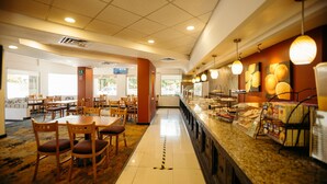 Un restaurante con una barra larga, varias mesas y sillas. Hay luces en el techo y suelo de baldosas.