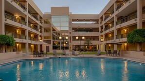 Un hotel de varios pisos con una piscina central, mobiliario exterior e un atrio bien iluminado.