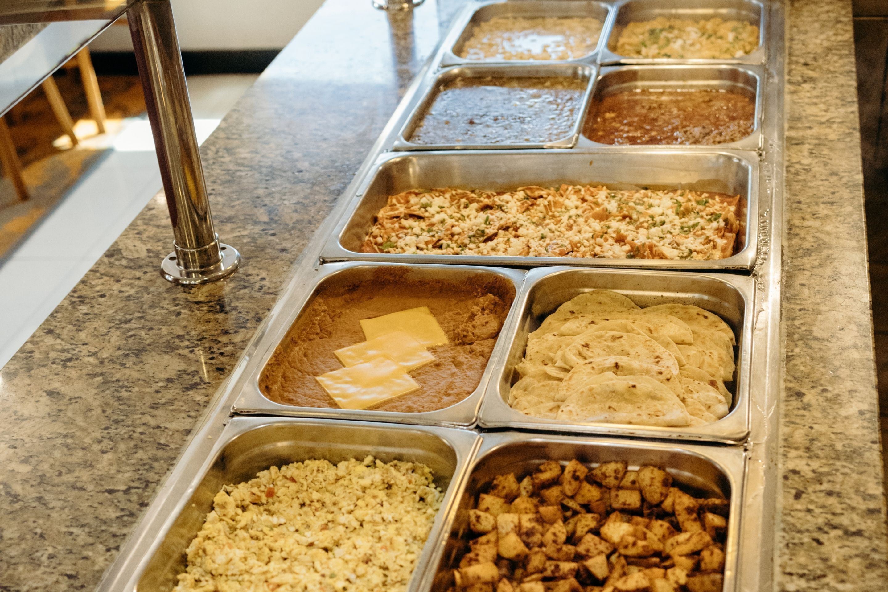 Un bufé con diversas opciones de comida en bandejas metálicas.