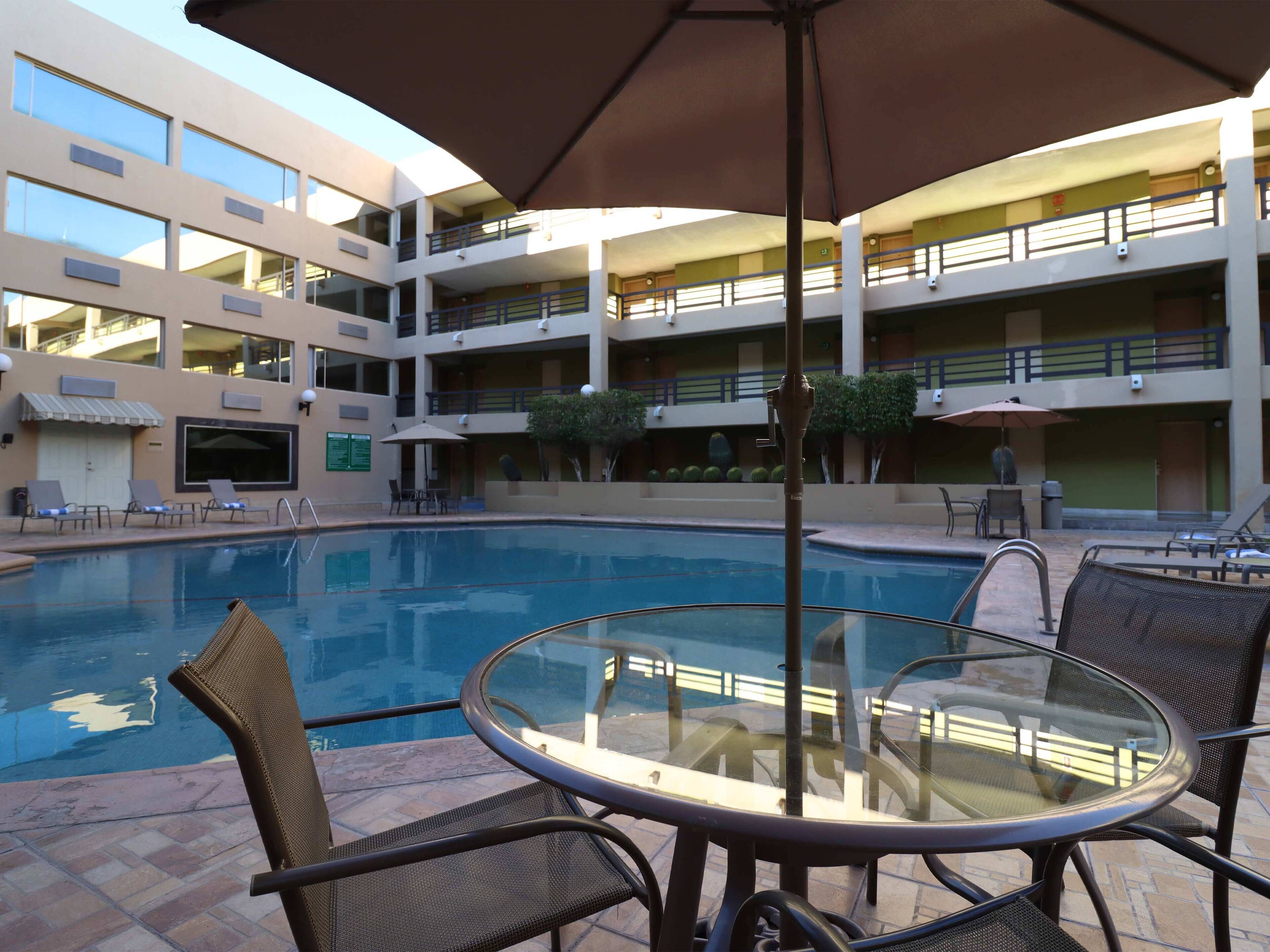 A pool area with a glass table and chairs, surrounded by a multi-level building with balconies and outdoor seating.