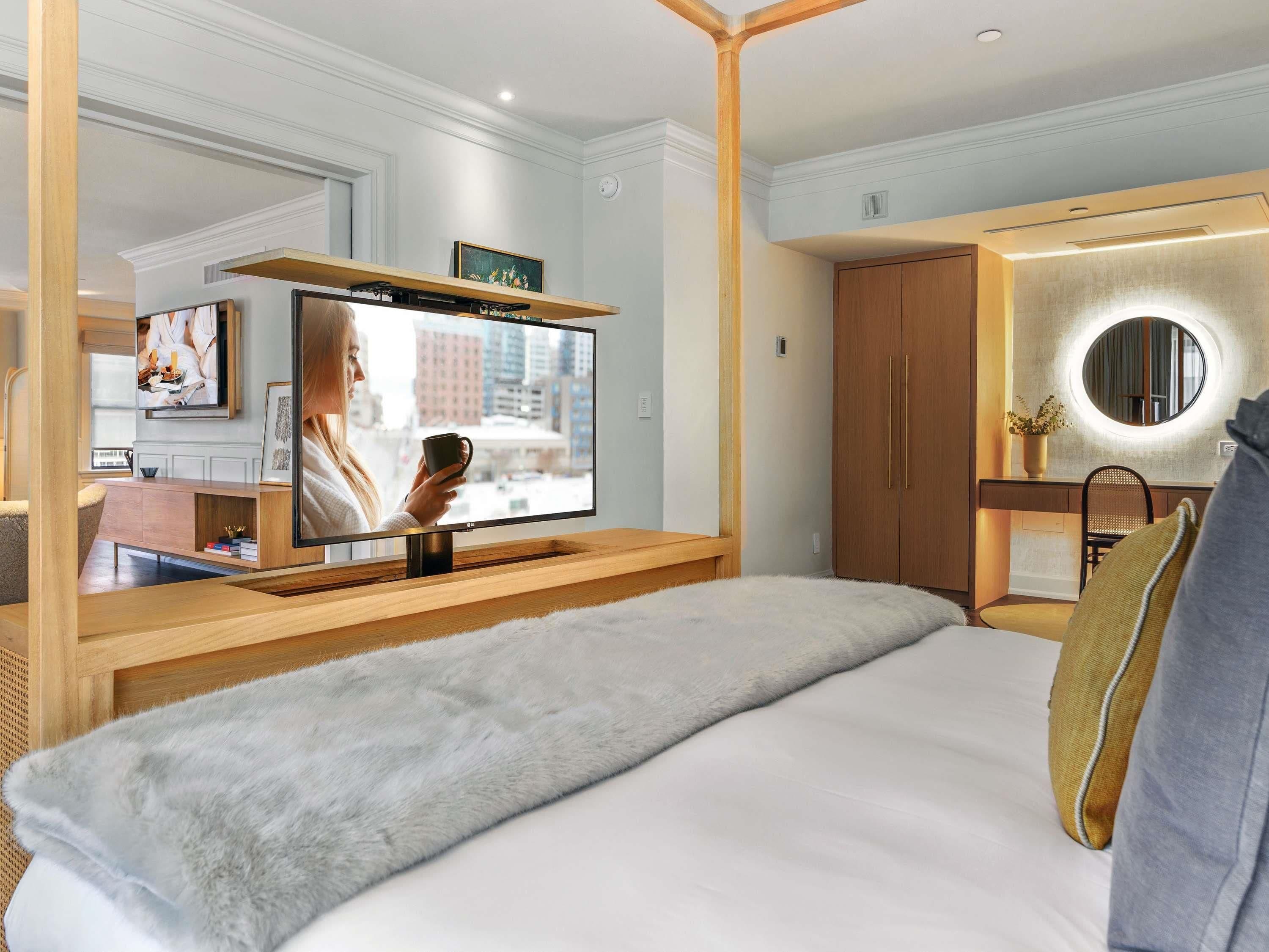 Una habitación de hotel con una cama, televisión, espejo y un armario de madera.