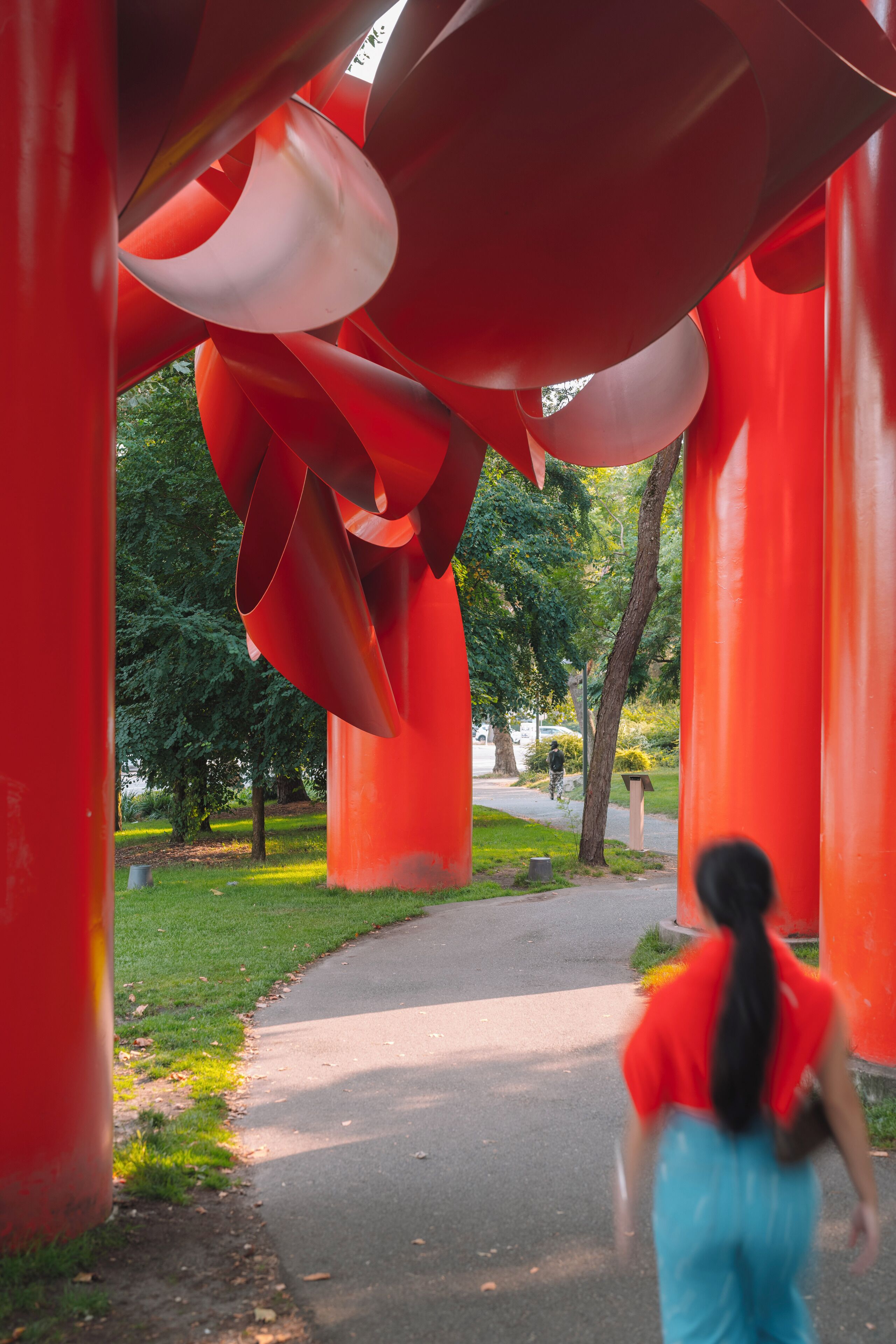 A pathway under large red structures, with a person walking away.