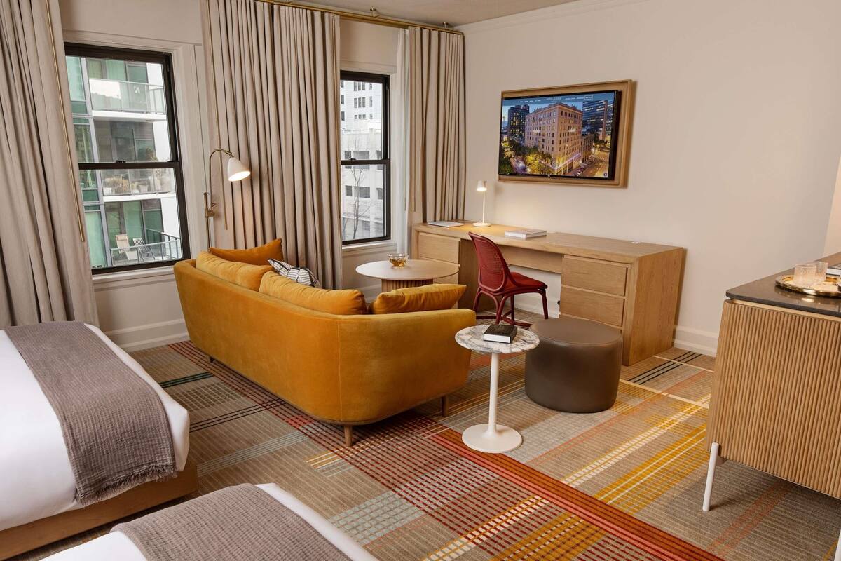 Habitación de hotel con sofá, escritorio, silla, cama y vista a la ciudad a través de la ventana.