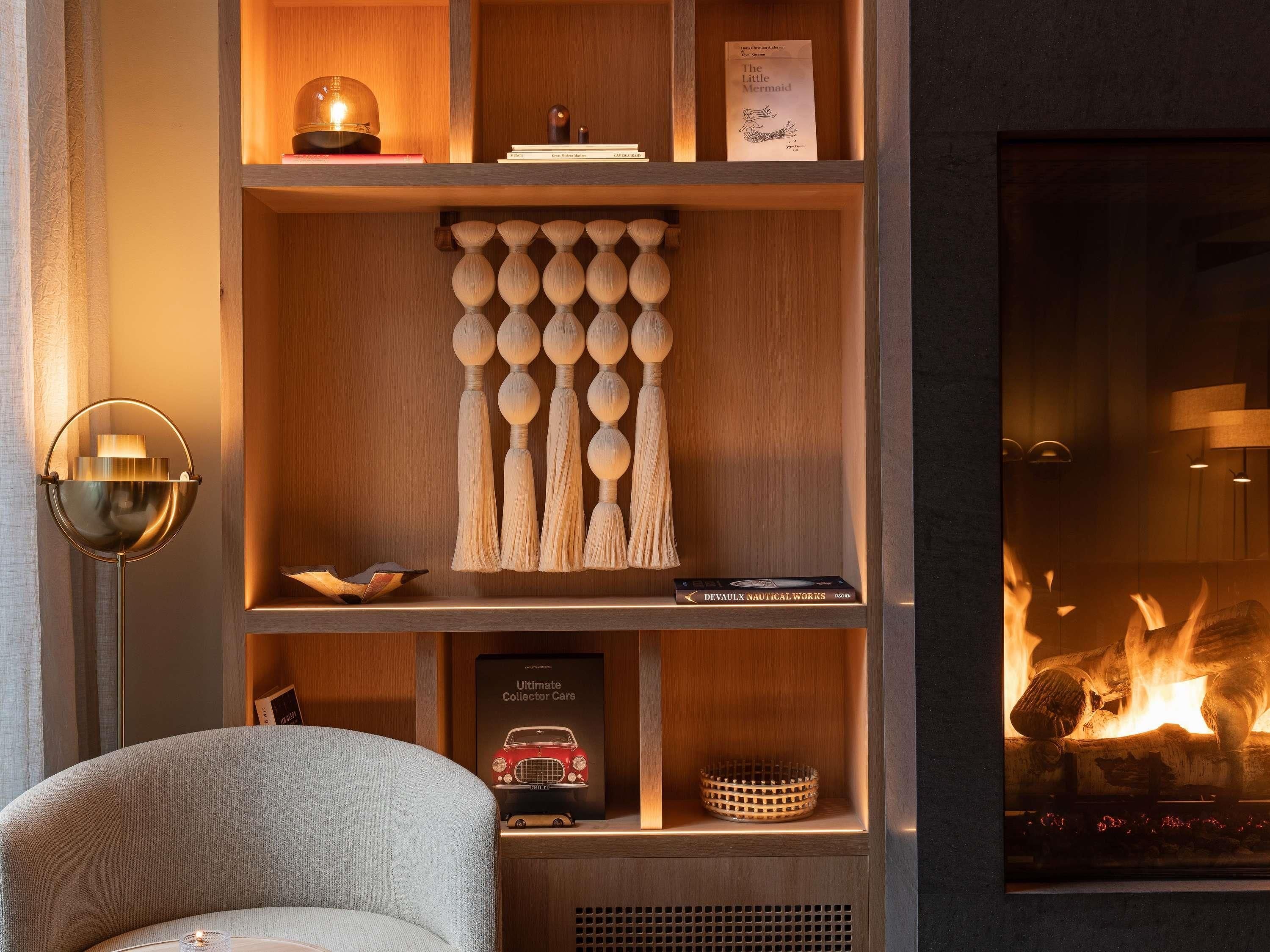 Ein gemütliches Zimmer mit Kamin, einem Bücherregal mit Büchern und Dekoration, einer Lampe und einem Sessel.