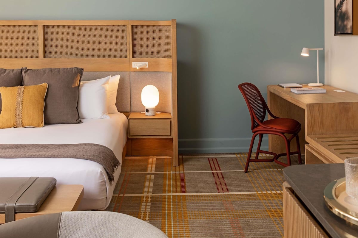 Habitación de hotel con cama, mesita de noche, lámpara, escritorio, silla y una pequeña mesa con bandeja.