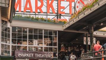 Um mercado público movimentado com um letreiro grande que diz 'PUBLIC MARKET', um teatro no mercado e uma escadaria com grafites.