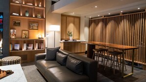 A modern living room with a leather sofa, a wooden bookshelf, a dining area with stools, and a kitchen in the background. - Ändra Hotel Seattle - MGallery Collection (Seattle)