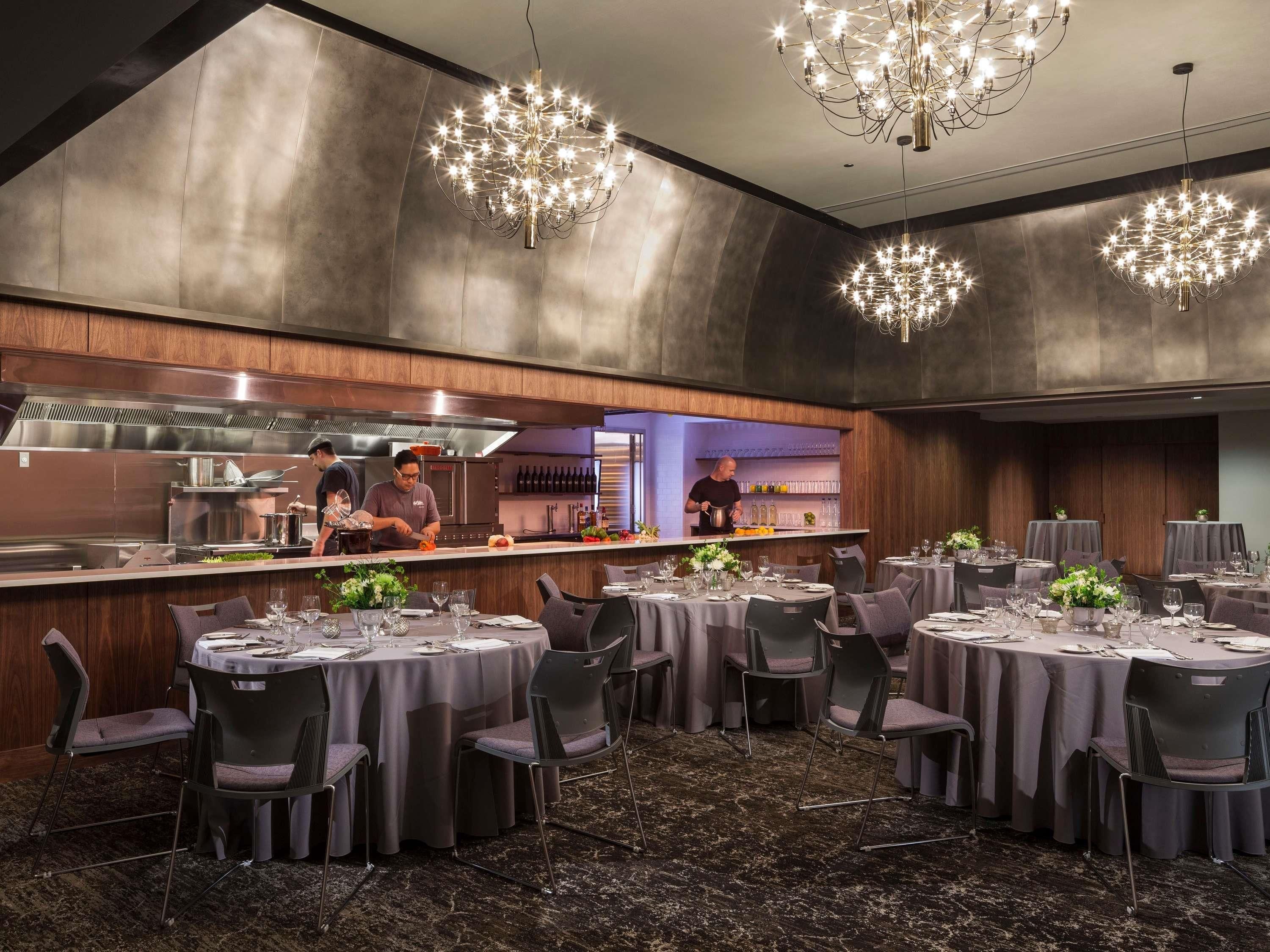 A restaurant with round tables, a bar, and a kitchen in the background.