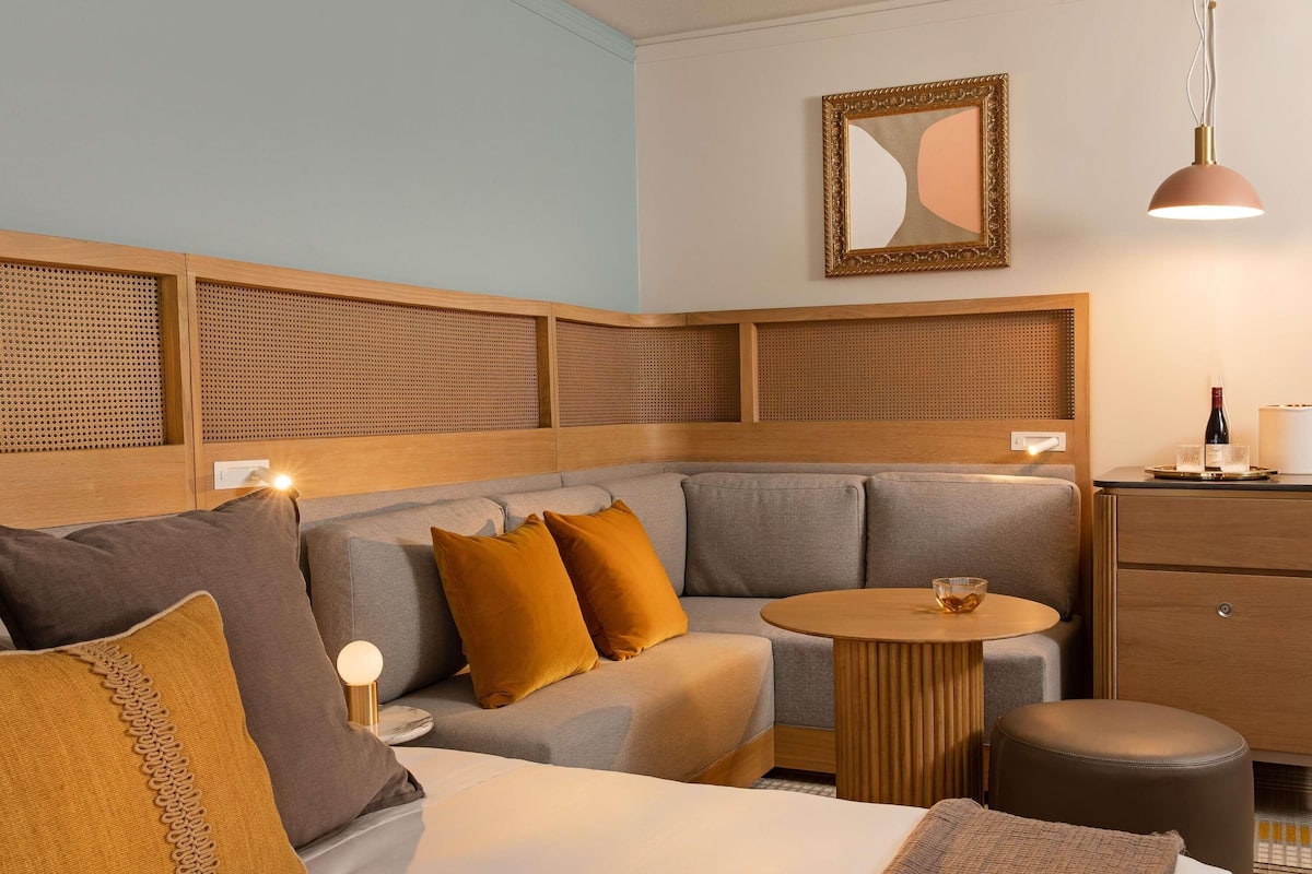 Una habitación de hotel moderna con sofá, una mesita redonda, cama y un armario de madera.