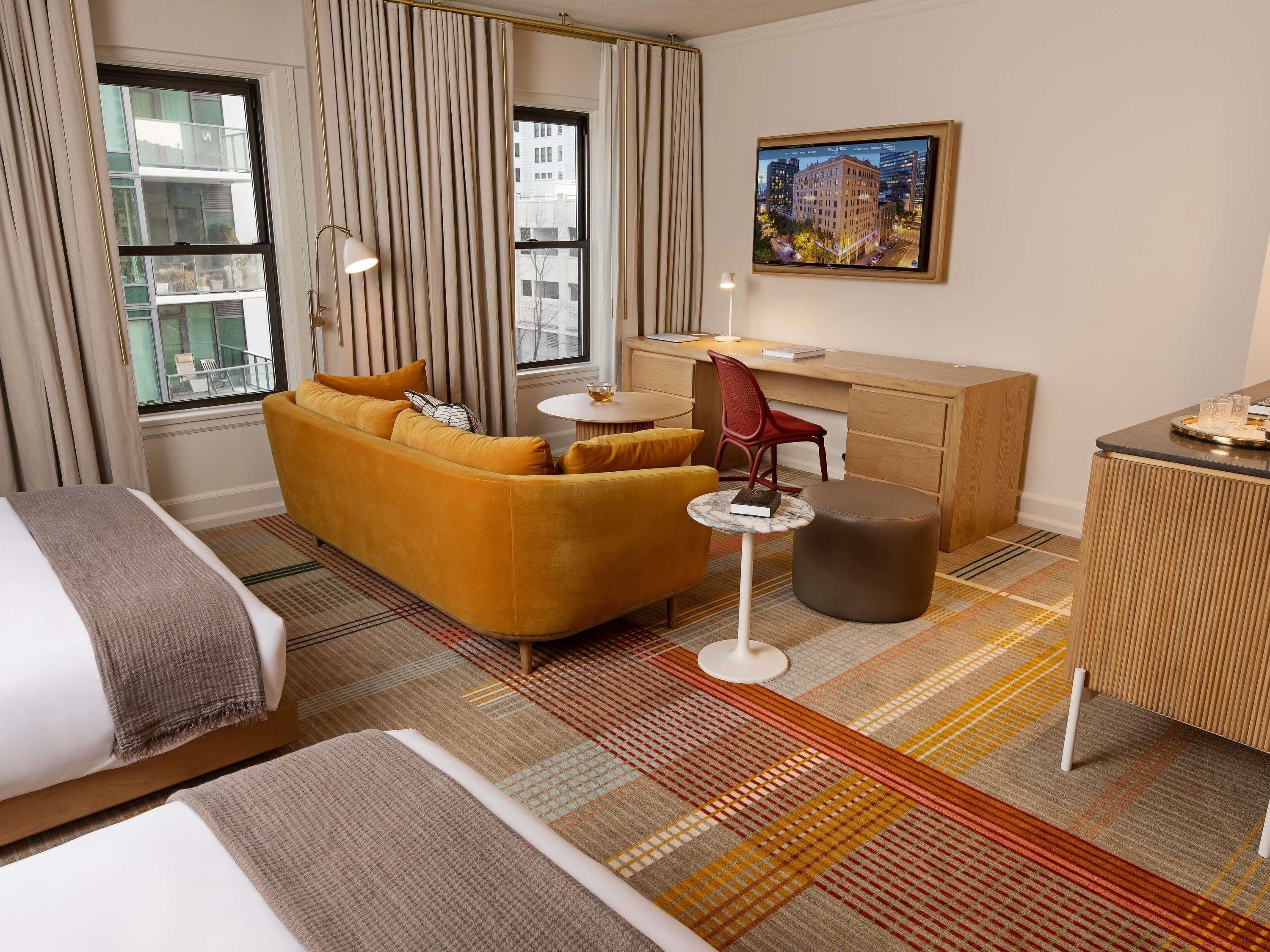 Quarto de hotel com sofá, escrivaninha, cadeira, cama e vista para a cidade pela janela.
