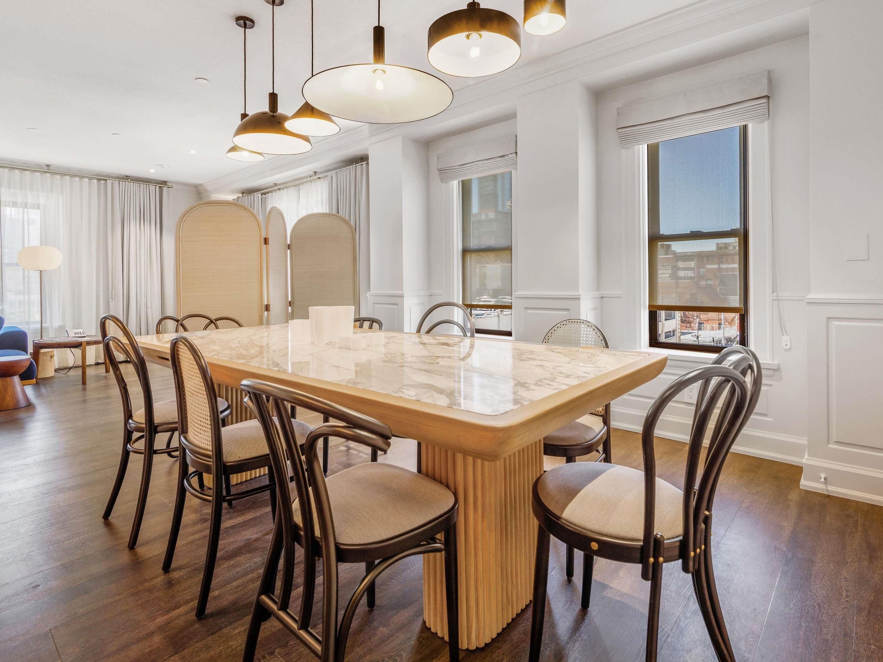 A dining area with a marble table, upholstered chairs, pendant lighting, and large windows with a city view.