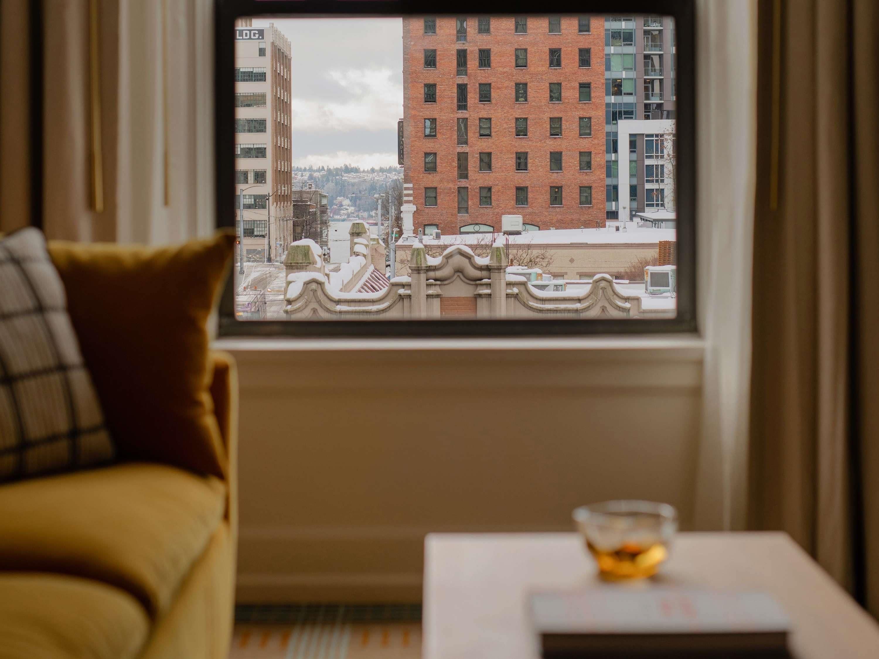 A room with a view of a cityscape through a window, a sofa, and a small table with a bowl.
