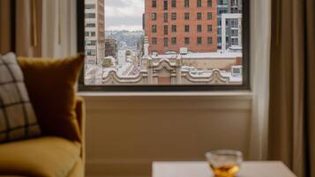 A room with a view of a cityscape through a window, a sofa, and a small table with a bowl.