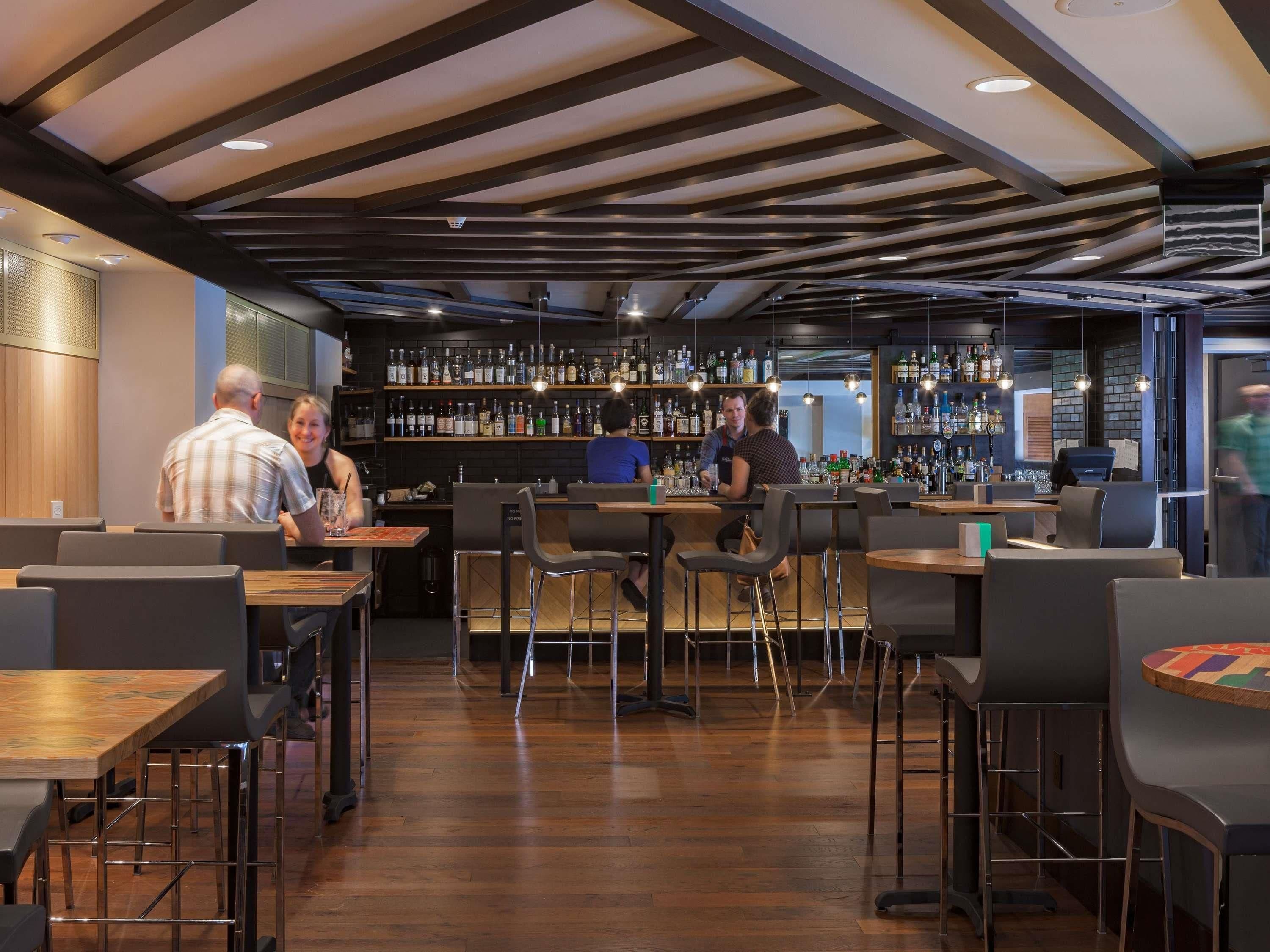 A modern bar area with wooden floors, metal bar stools, and a variety of liquor bottles on shelves.