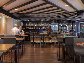 A modern bar area with wooden floors, metal bar stools, and a variety of liquor bottles on shelves.